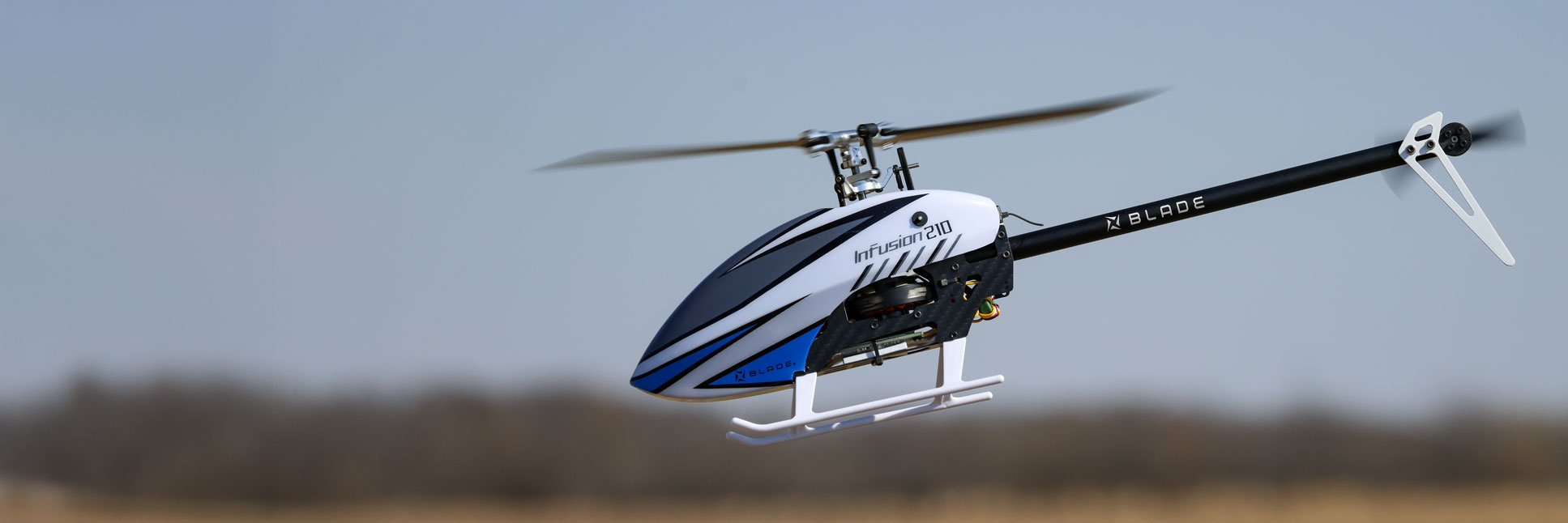 Action shot of the Blade® InFusion 210 Bind-N-Fly Basic with AS3X and SAFE RC helicopter hovering in the air above a field