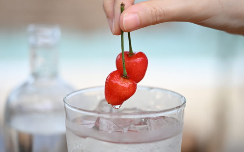 Close focus shown in a photo of cherries held over a glass of liquid, in a photo taken with the NIKKOR Z 24-70mm f/2.8 S II