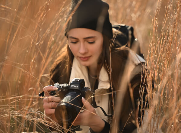 A female photographer holds the Z5II while crouched in a field of tall amber grasses.