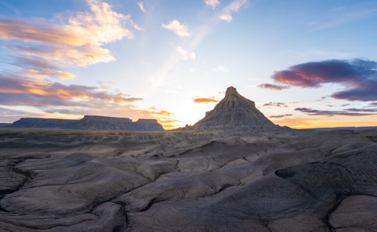 A colorful, cloud-filled sky spans over the open terrain of the American Southwest with mesas and buttes in the distance.
