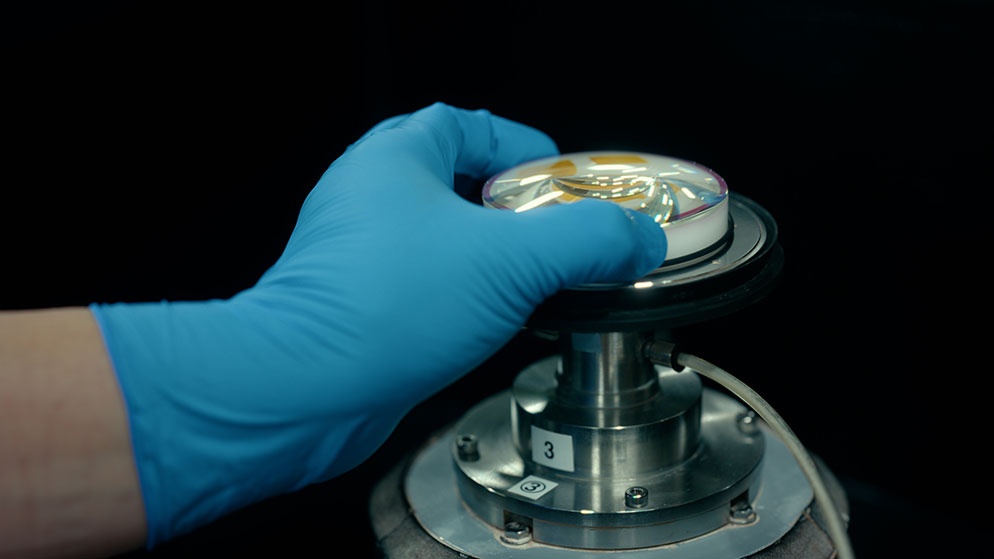 photo of a gloved hand holding a piece glass to become a lens element