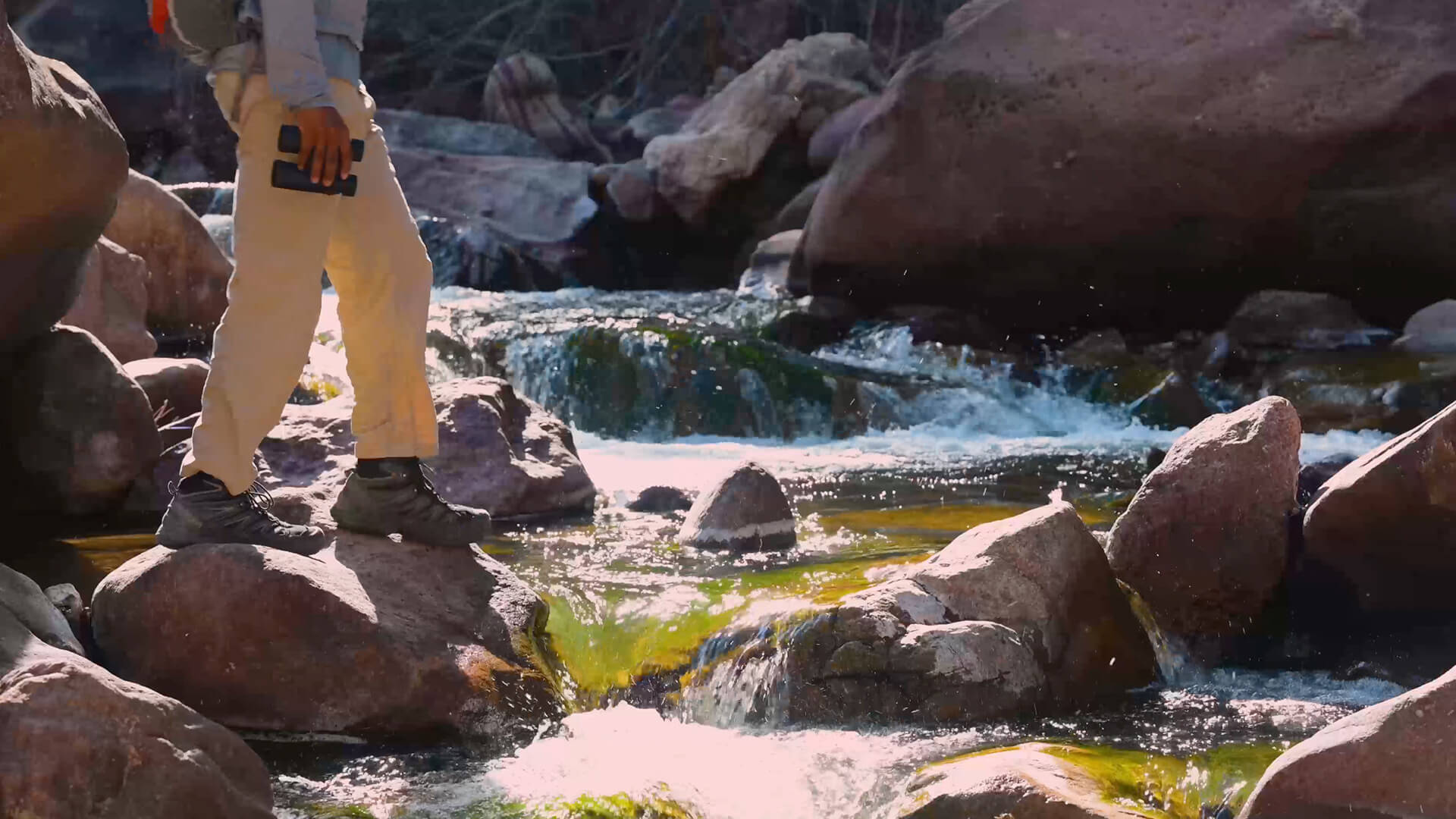 Person crossing a stream while holding a pair of Prostaff P3 binoculars
