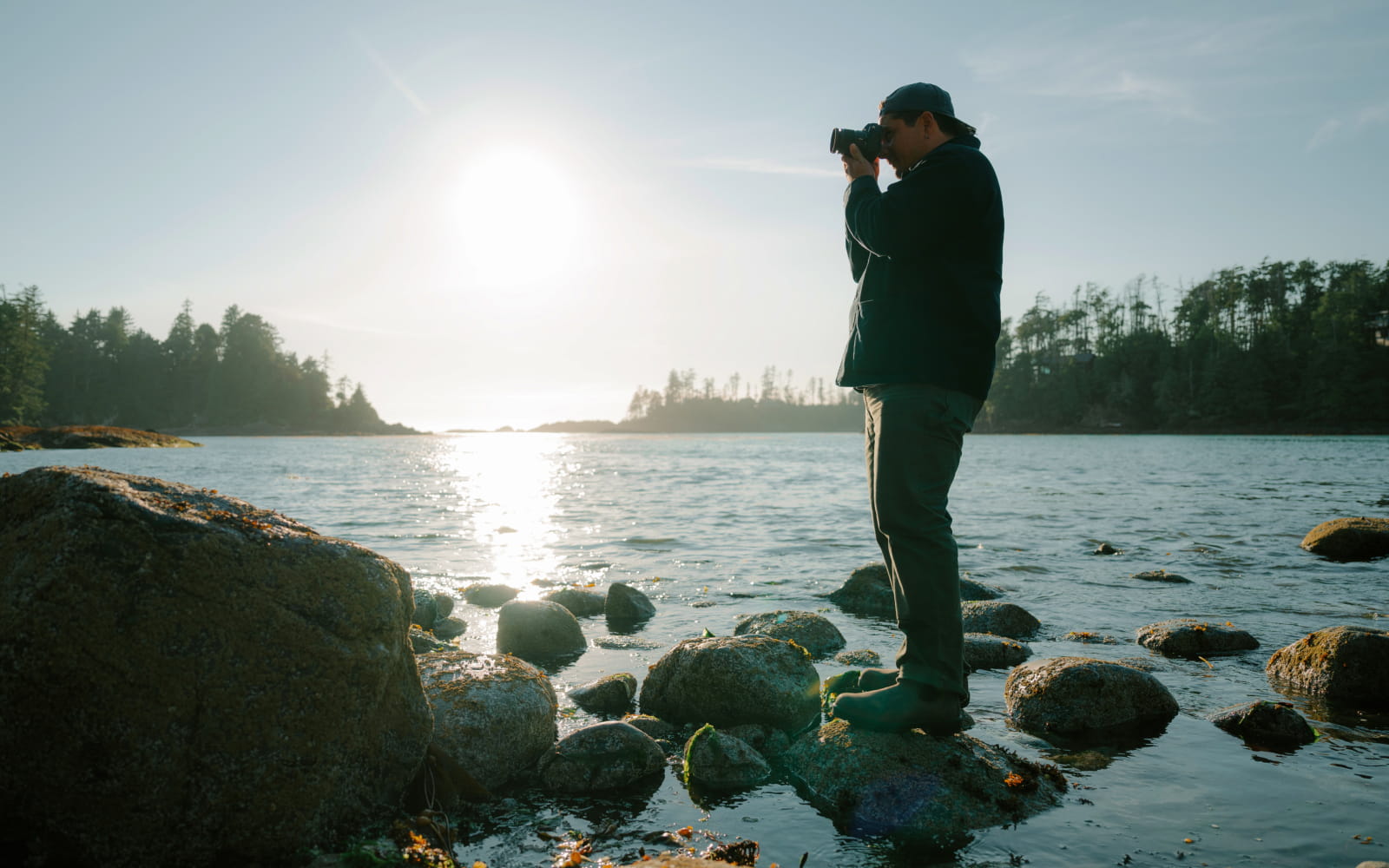photo of a man standing on rocks in a lake taking a photo, shot with the NIKKOR Z DX MC 35mm f/1.7 lens