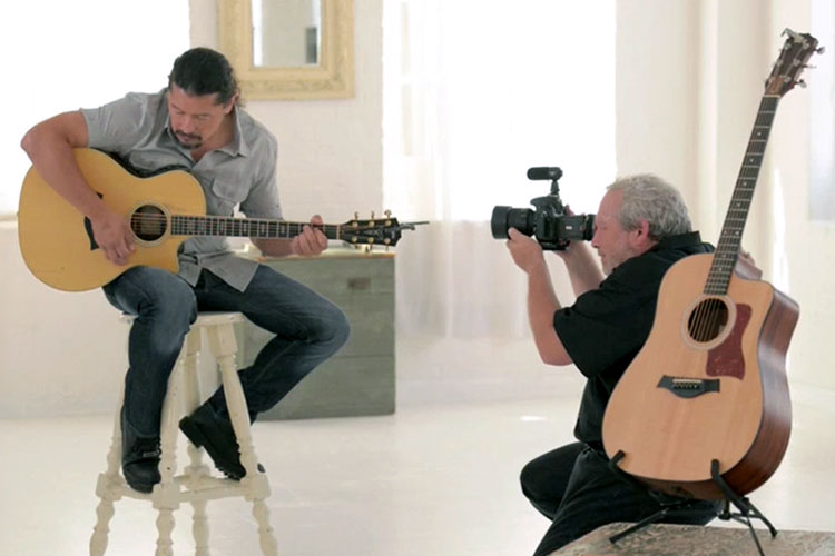 A videographer records a man playing an accoustic guitar
