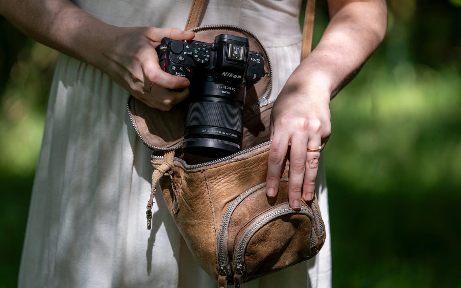 photo of a woman putting a camera and NIKKOR Z DX MC 35mm f/1.7 lens into a purse