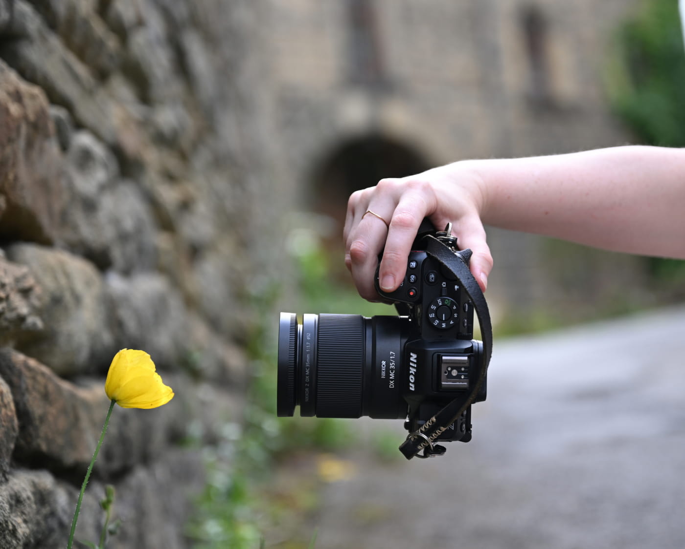photo of a person's hand holding a camera photographing a yellow flower with the NIKKOR Z DX MC 35mm f/1.7 lens