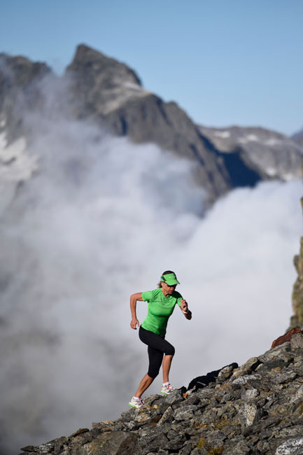 A woman in green athletic grear runs up a rock covered mountain