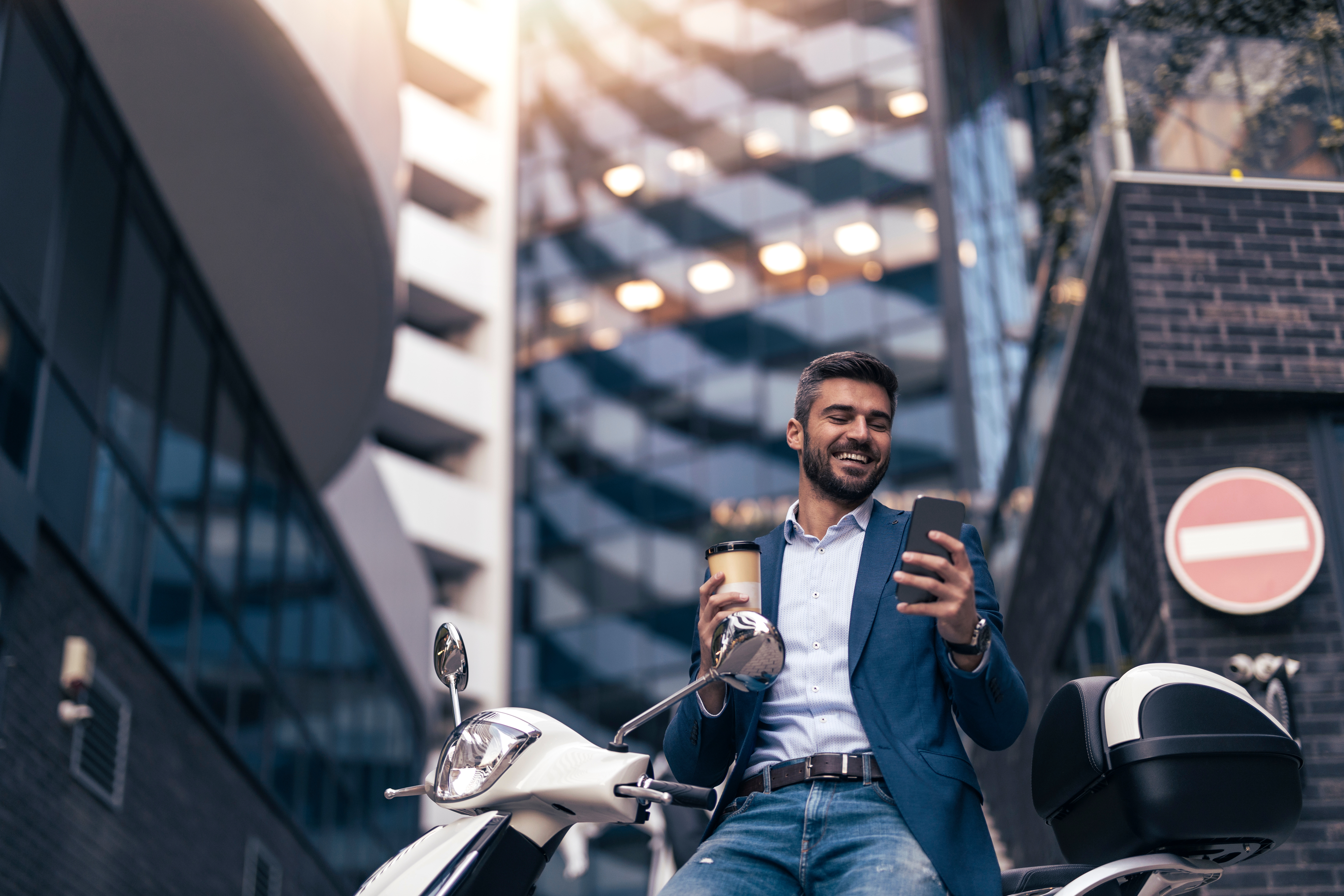 Image of man smiling with coffee and iphone by a motorcycle