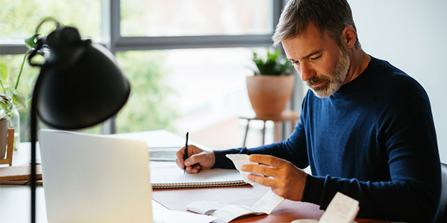 Man viewing receipts and documenting his expenses in a spiral notebook