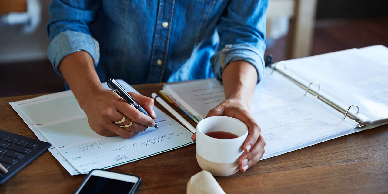 A man drinking coffee and taking notes about a financial plan.