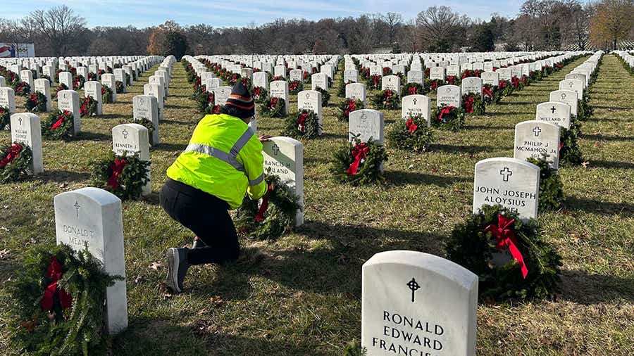 Schneider driver kneeling down to lay a wreath at the gravesite of a deceased veteran with several rows of headstones 