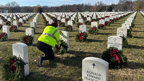 Schneider driver kneeling down to lay a wreath at the gravesite of a deceased veteran with several rows of headstones