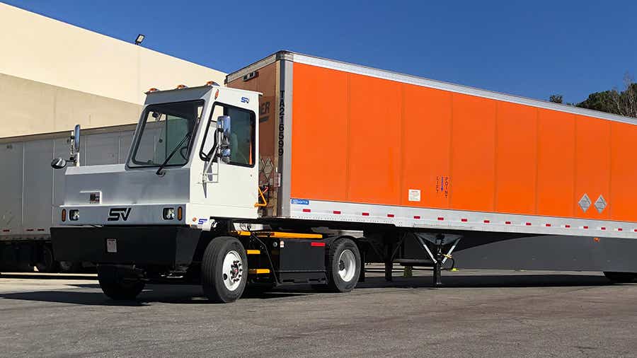 One of Schneider's electric terminals trucks moves an orange Schneider trailer through the yard