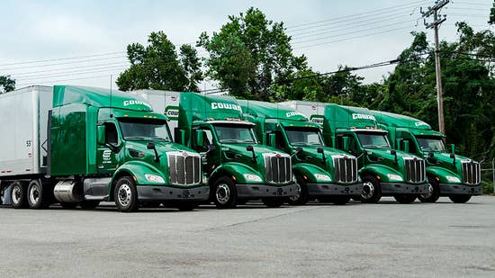 Five green Cowan semi trucks with white Cowan trailers parked in a row