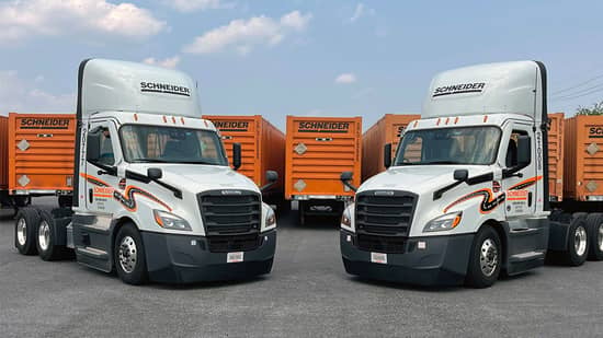 Two Schneider Intermodal day cabs parked nose to nose in front of a row of orange Schneider Intermodal containers