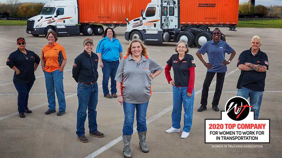 A group of Schneider women truck drivers stand proudly in front of a Schneider tractor, container and day cab