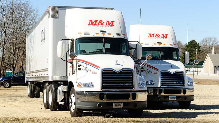 Two M&M Transport trucks parked in an unpaved parking lot