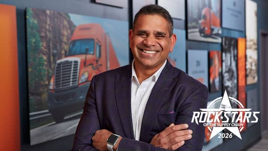 Haroon Syed stands in front of a historical wall of Schneider truck photos at the Schneider headquarters 