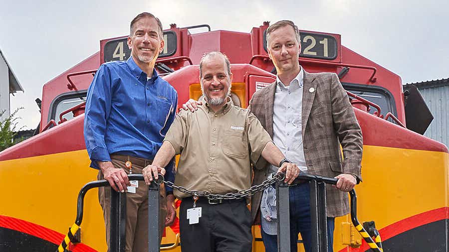 John Bozec, Bernardo Rodarte and Michael Baumgardt stand in front of a large, yellow and red locomotive in Mexico.