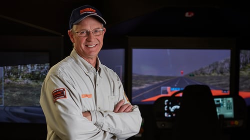A Schneider driver instructor standing with his arms crossed in front of the driving simulator 