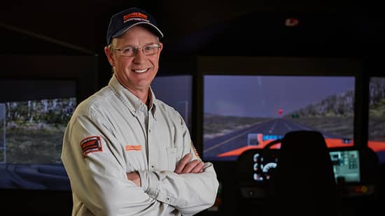 driver instructor roles_sep2026_hero.jpg Schneider driver instructor standing with his arms crossed in front of the driving simulator