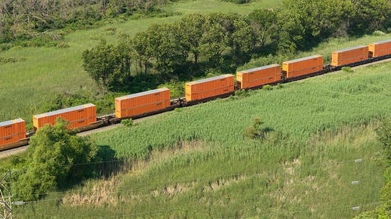 Aerial view of a train with Schneider containers traveling through a green, grassy landscape with trees in the background