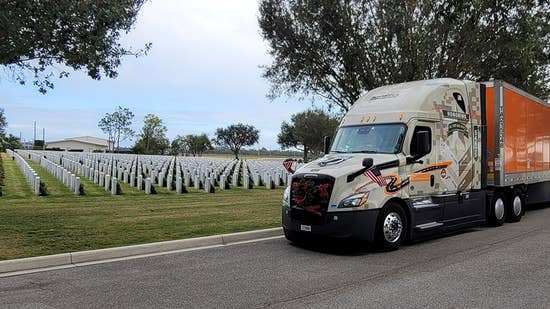 wreaths across america 2025_hero.jpg Schneider military theme wrapped trucks hauling an orange trailer parked in a military cemetery next to headstones