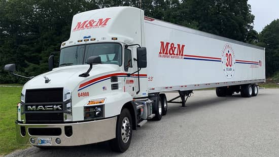 An M&M Transport Services truck and trailer parked on the side of the road
