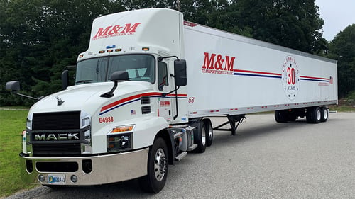 An M&M Transport Services truck and trailer parked on the side of the road