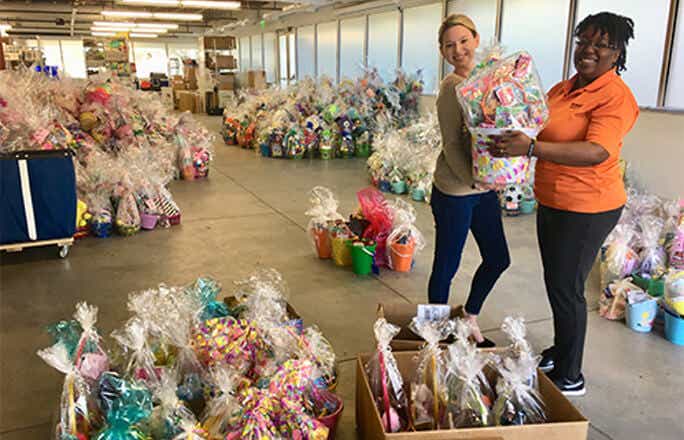 Image of Schneider associates holding gift baskets in a storage area of hundreds of gift baskets