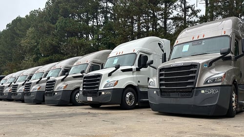 A row of several Freightliner Cascadias in the lot of a Schneider facility as part of Schneider's used equipment sales.