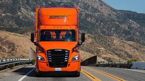 A front-facing look at an orange Schneider Freightliner eCascadia as it drives down the highway in California.