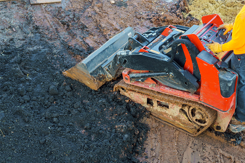 Worker moving dirt with a mini skid steer loader