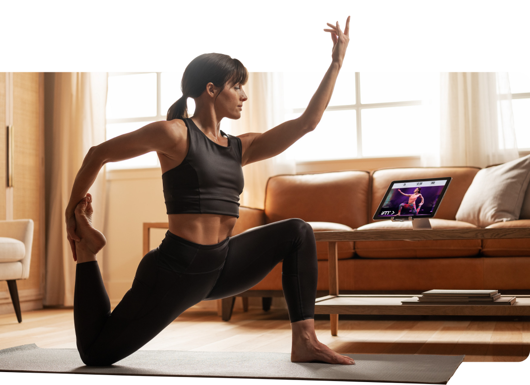 Woman does yoga pose while watching iFIT on tablet
