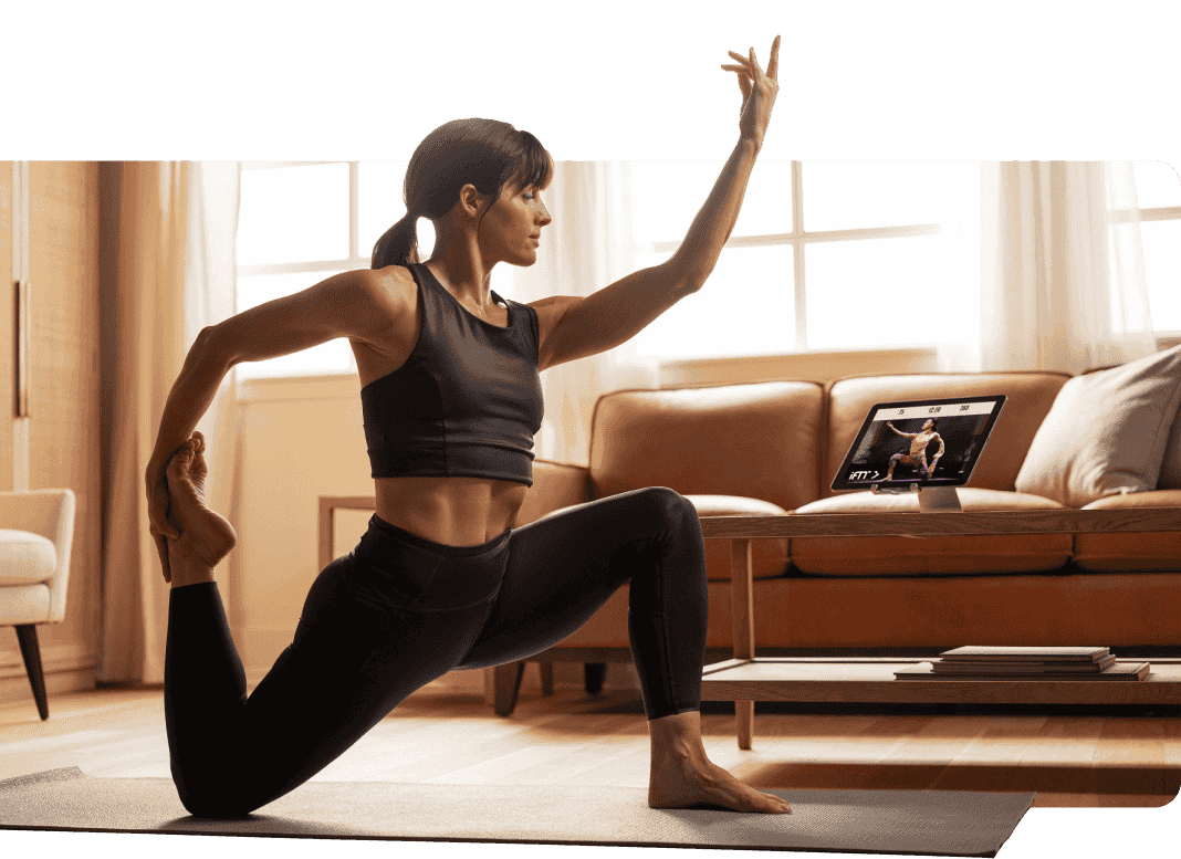 Woman does yoga pose while watching iFIT on tablet