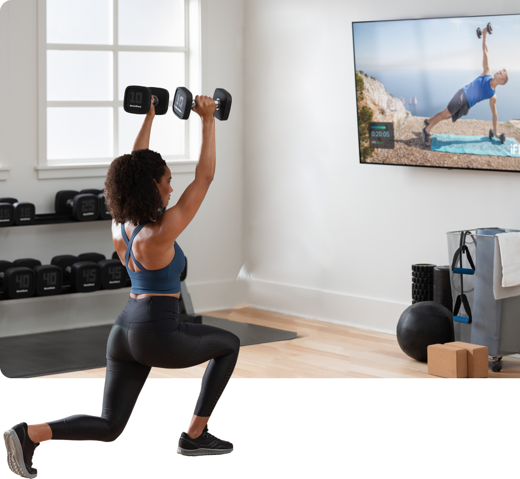 Woman exercises with dumbells while watching iFIT on TV