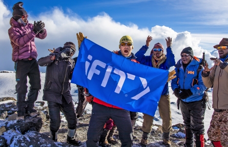 Group of people on top of mountain holding iFIT flag