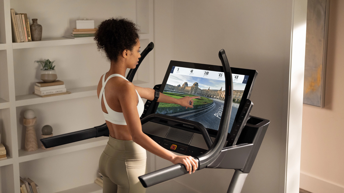 Woman touches her iFIT-enabled treadmill’s screen during a running workout