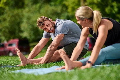A couple stretches together outdoors on yoga mats using the Anytime Fitness app