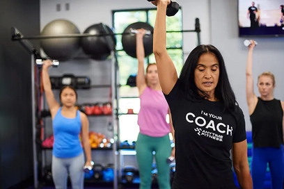 An Anytime Fitness coach leads a class using dumbbells