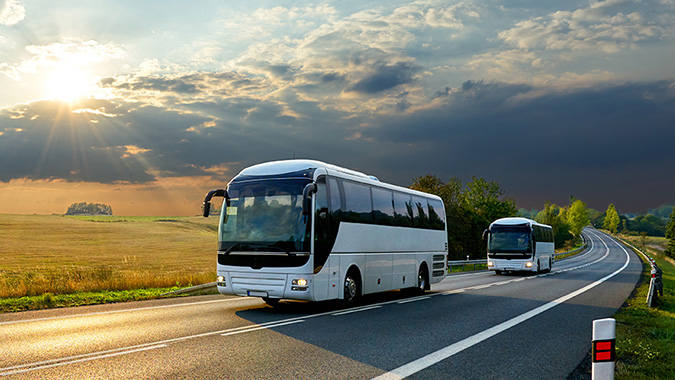 Two motorcoaches driving on a empty stretch of road.