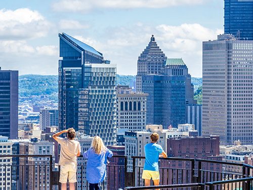 Three people stand at a look out point and look over the city scape of Pittsburgh city 