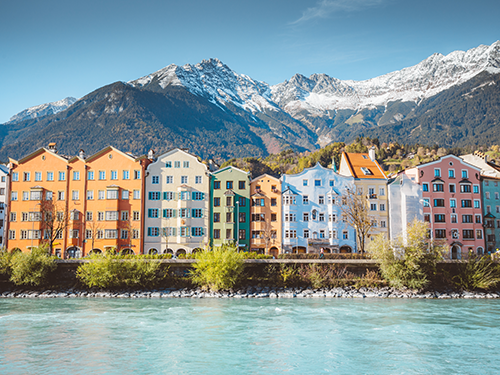 The mountain range around Innsbruck pictured with coloured houses and water in the foreground.