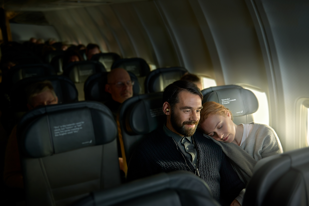 A woman cuddling up to a man on an Icelandair plane, traveling together.