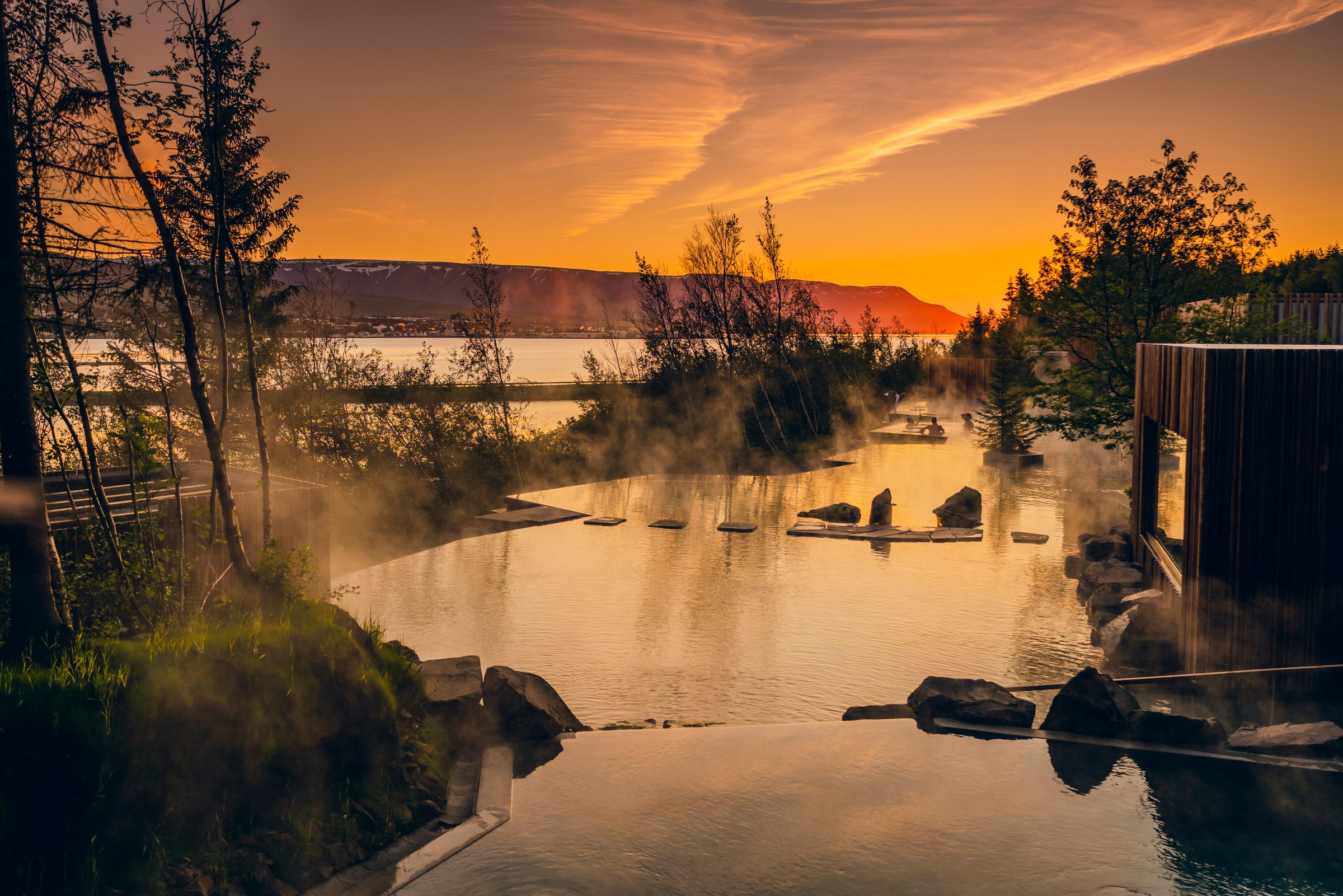 The Forest Lagoon geothermal baths: a warm pool set amid trees, with a view of sunset over Eyjafjörður