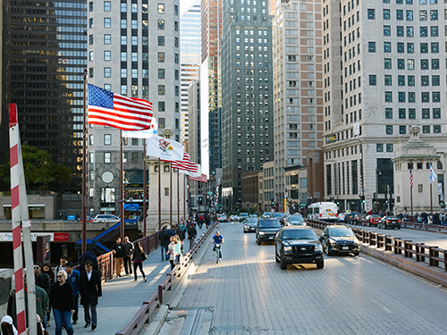 The American flag flies above a bridge in Chicago, with traffic streaming towards the camera 