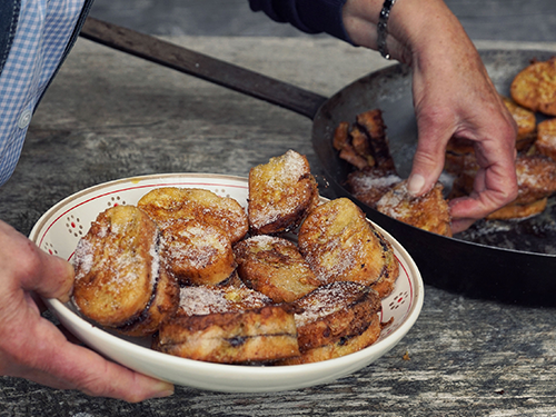 Two hands handling pofosen, which are soft dough-like sweet bites, from pan to plate 