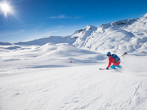A person in a red jacket and blue trousers skiing down the slopes in Zurich, Switzerland 