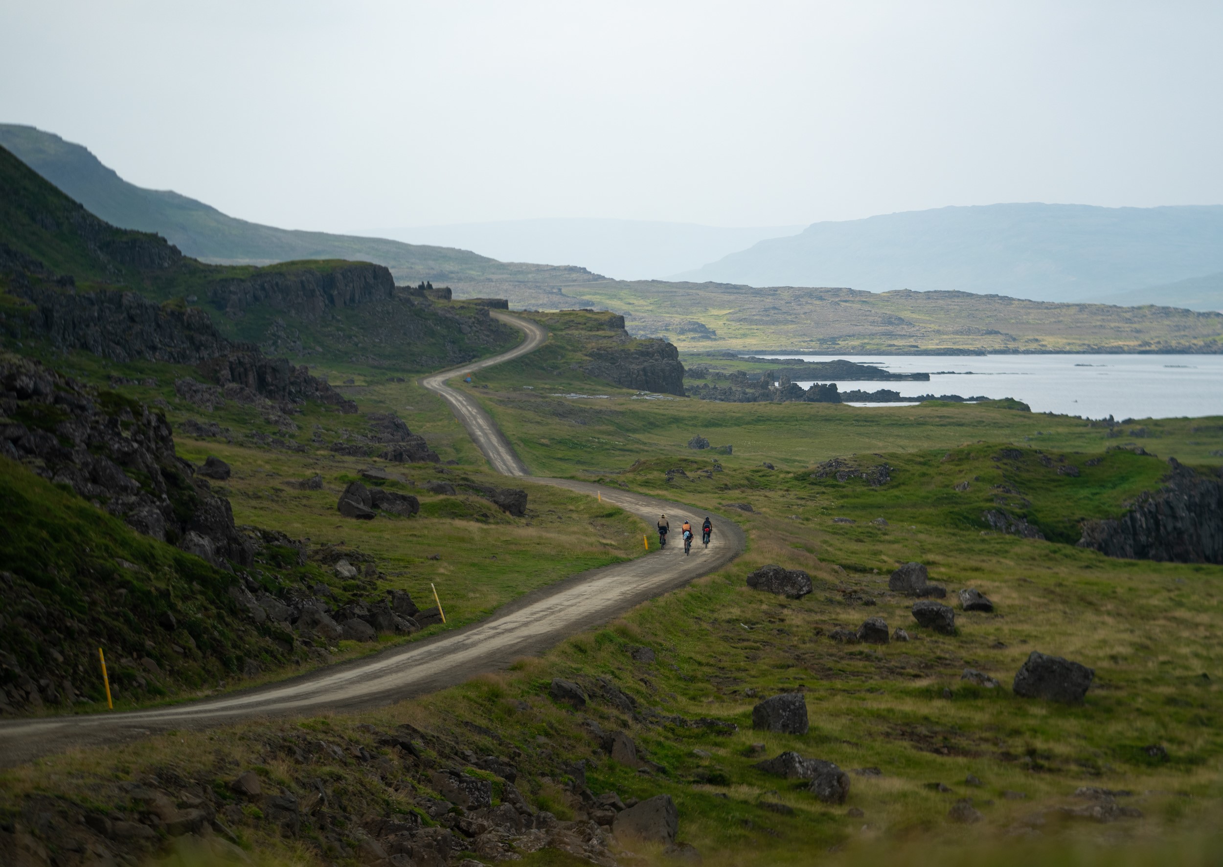 Cyclists on a gravel road by the edge of a fjord in the Westfjords