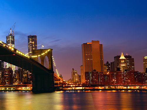 Brooklyn Bridge in New York pictured in evening light with the city lights bright against the night sky 